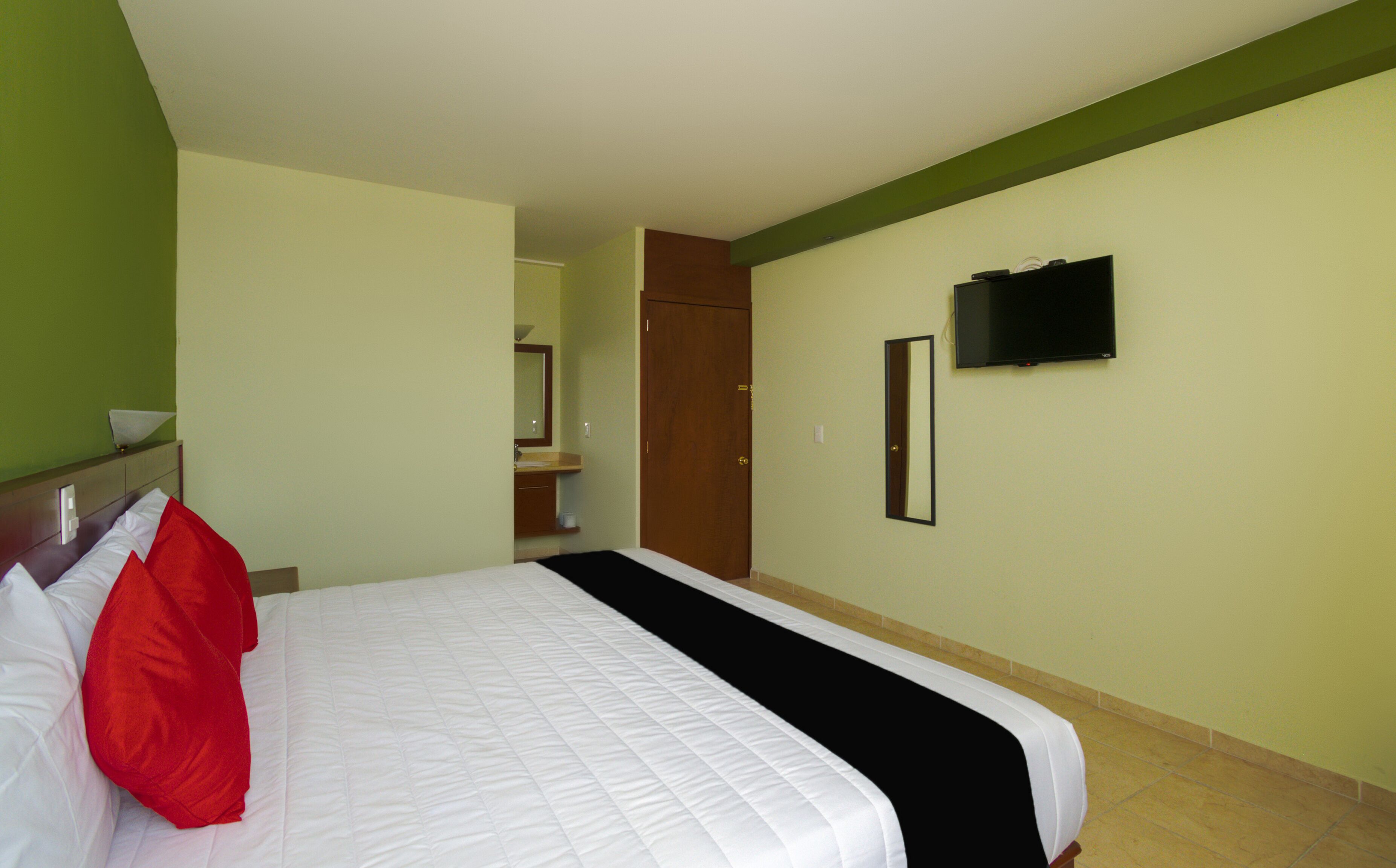 A hotel room with a bed, a television mounted on the wall, and a door leading to a bathroom.