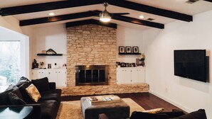A living room with a stone fireplace, dark wooden beams, white cabinets, and a flat-screen TV mounted on the wall. - SXSW House near iconic Barton Springs (Austin)
