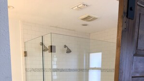 A glass-enclosed shower with white tiles and a small shelf with toiletries. - SXSW House near iconic Barton Springs (Austin)