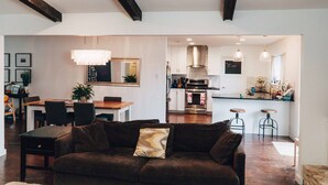 A modern living room with a dark brown sofa, a dining area with a wooden table and chairs, and a kitchen with white cabinets and a stainless steel oven. - SXSW House near iconic Barton Springs (Austin)
