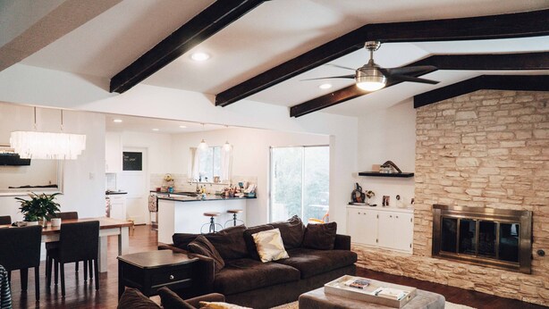 A spacious living room with a stone fireplace, dark wooden furniture, and a modern kitchen in the background. - SXSW House near iconic Barton Springs (Austin)