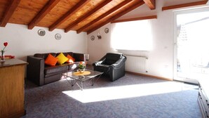 A cozy living room with a wooden ceiling, a sofa with colorful cushions, a leather armchair, and a glass coffee table. - Casa Esmeralda GIOIA - 2-room apartment, approx. 45 m², with small balcony (Gambarogno)
