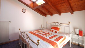 A bedroom with a wooden ceiling, a bed with a striped bedspread, a bedside table with a lamp, and a small shelf with a book. - Casa Esmeralda GIOIA - 2-room apartment, approx. 45 m², with small balcony (Gambarogno)