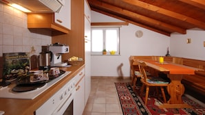 A kitchen with wooden cabinets, a stove, and a dining table with chairs. - Casa Esmeralda GIOIA - 2-room apartment, approx. 45 m², with small balcony (Gambarogno)