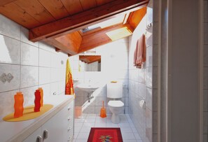 A bathroom with a skylight, white tiles, a sink, toilet, and a red rug. - Casa Esmeralda GIOIA - 2-room apartment, approx. 45 m², with small balcony (Gambarogno)