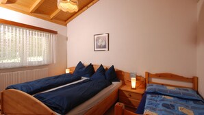 A double bed with a wooden headboard, a bedside table with a lamp, and a window with curtains. - Casa Esmeralda SERENITA - 3-room apartment, approx. 65 m², with garden seating area (Gambarogno)