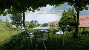 A table and chairs set outdoors with a view of a lake and mountains in the background. - Casa Esmeralda SERENITA - 3-room apartment, approx. 65 m², with garden seating area (Gambarogno)