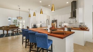 A spacious kitchen with a central island, bar stools, pendant lighting, and a piano in the adjacent room. - Wonderful New 3 Bedroom Villa , with direct Gluf Acces for your holidays (CAPE CORAL)