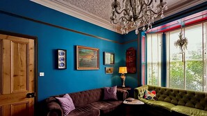 Une pièce avec un mur bleu, un canapé en cuir marron, un canapé vert, un tapis rouge à motifs et un lustre.