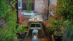 Une table en bois, ornée d’assiettes vertes, de bougies et d’une bouteille de champagne, entourée de plantes en pot et d’une lanterne.