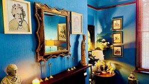Une pièce avec un mur bleu, un miroir, des tableaux encadrés, un buste, une bougie et une petite table ornée d’objets décoratifs.