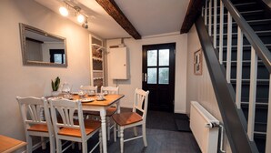 A dining area with a wooden table and white chairs, a built-in shelf with decorative items, and a staircase with a metal railing. - Gesindehaus Börnecke (Blankenburg)