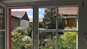 A room with a large window offering a view of a garden and neighboring buildings. - Gesindehaus Börnecke (Blankenburg)