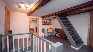 A staircase leading to a lofted area with a wooden beam ceiling, a rocking chair, a bookshelf, and a potted plant. - Gesindehaus Börnecke (Blankenburg)