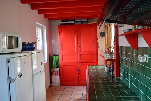 Una cocina compacta con un armario rojo, un refrigerador blanco y un microondas encima.