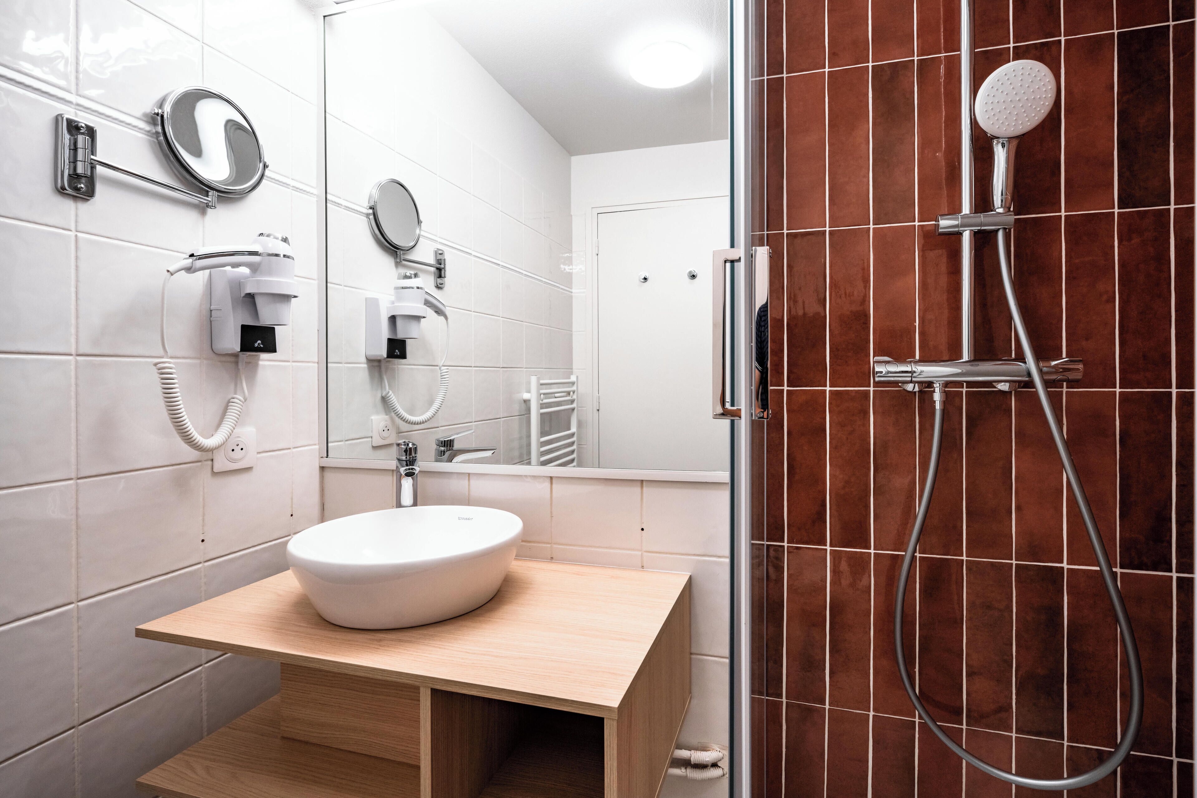 A modern bathroom with a round sink, a handheld showerhead, and a mirror.