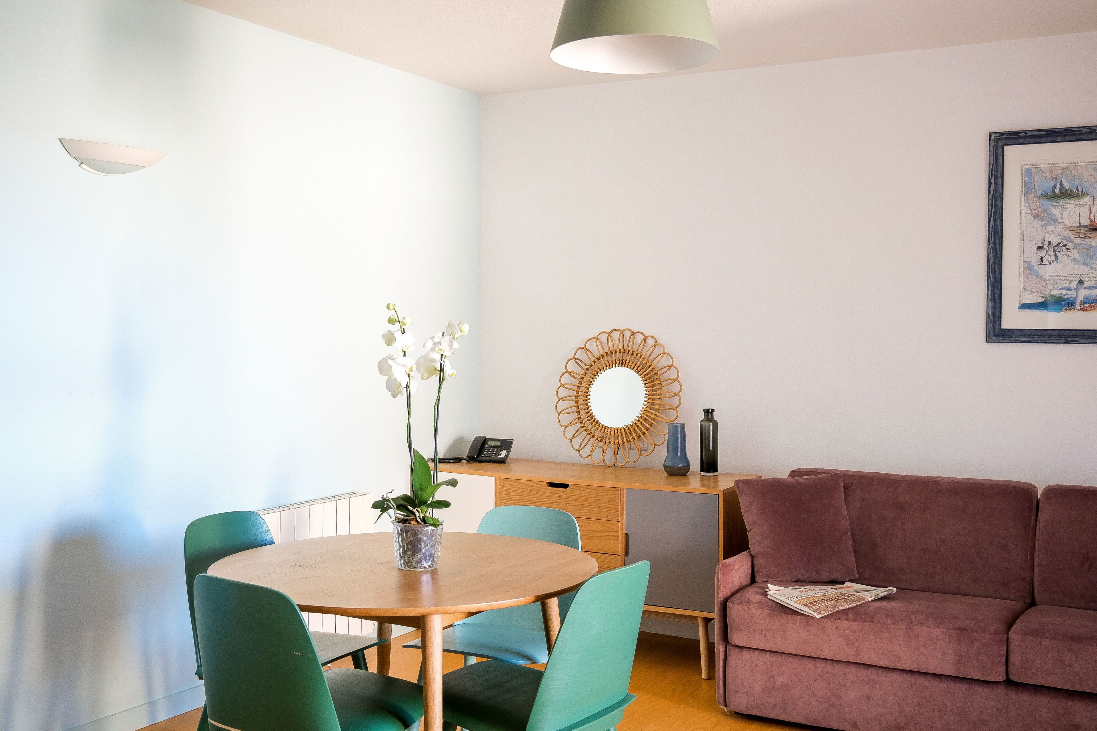 Un salon moderne avec une table ronde en bois, des fauteuils turquoise, un canapé rose et un grand miroir au mur.