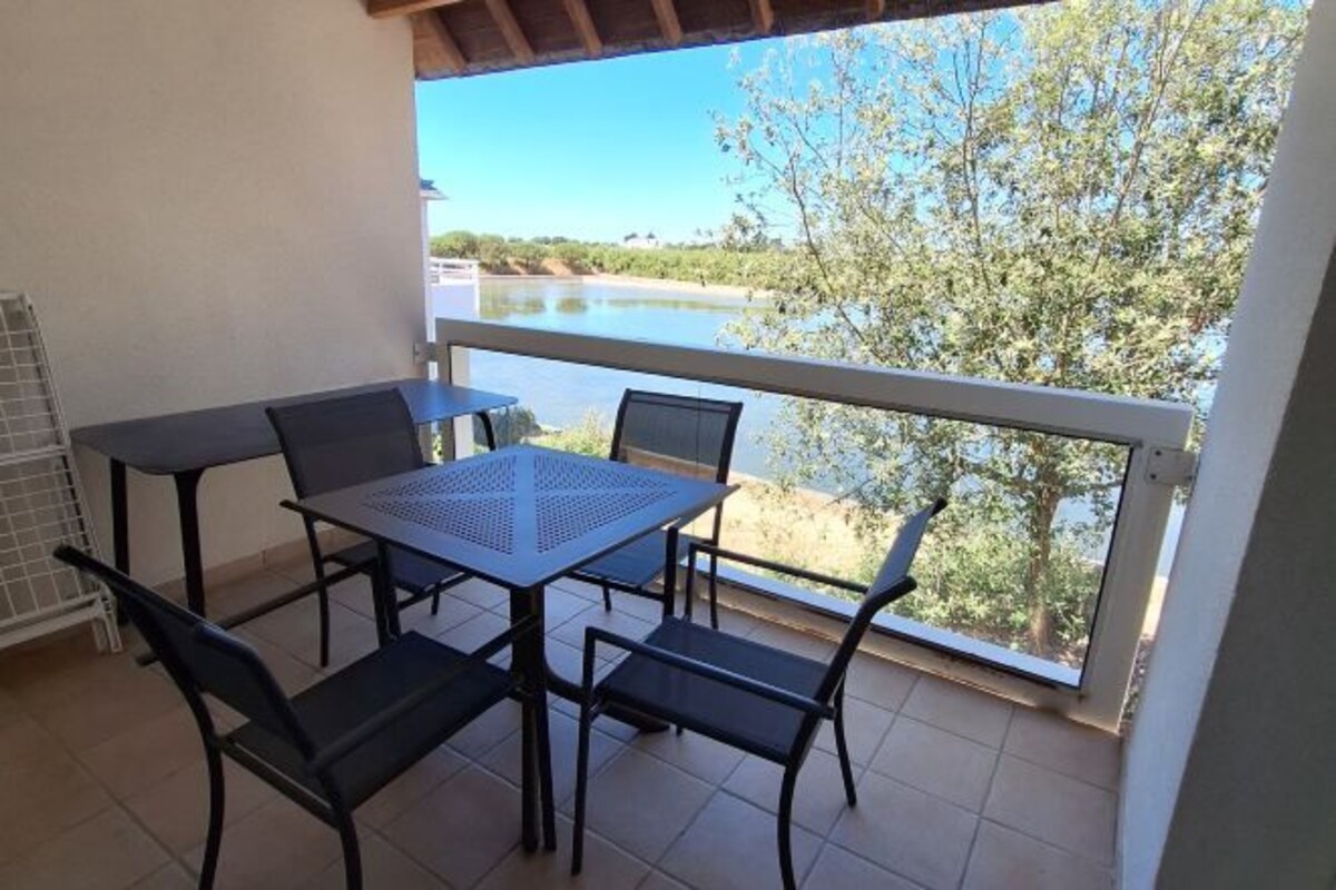 A balcony with a table and chairs, overlooking a body of water and greenery.