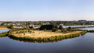 A lakeside view with a small island, houses in the distance, and a clear sky.
