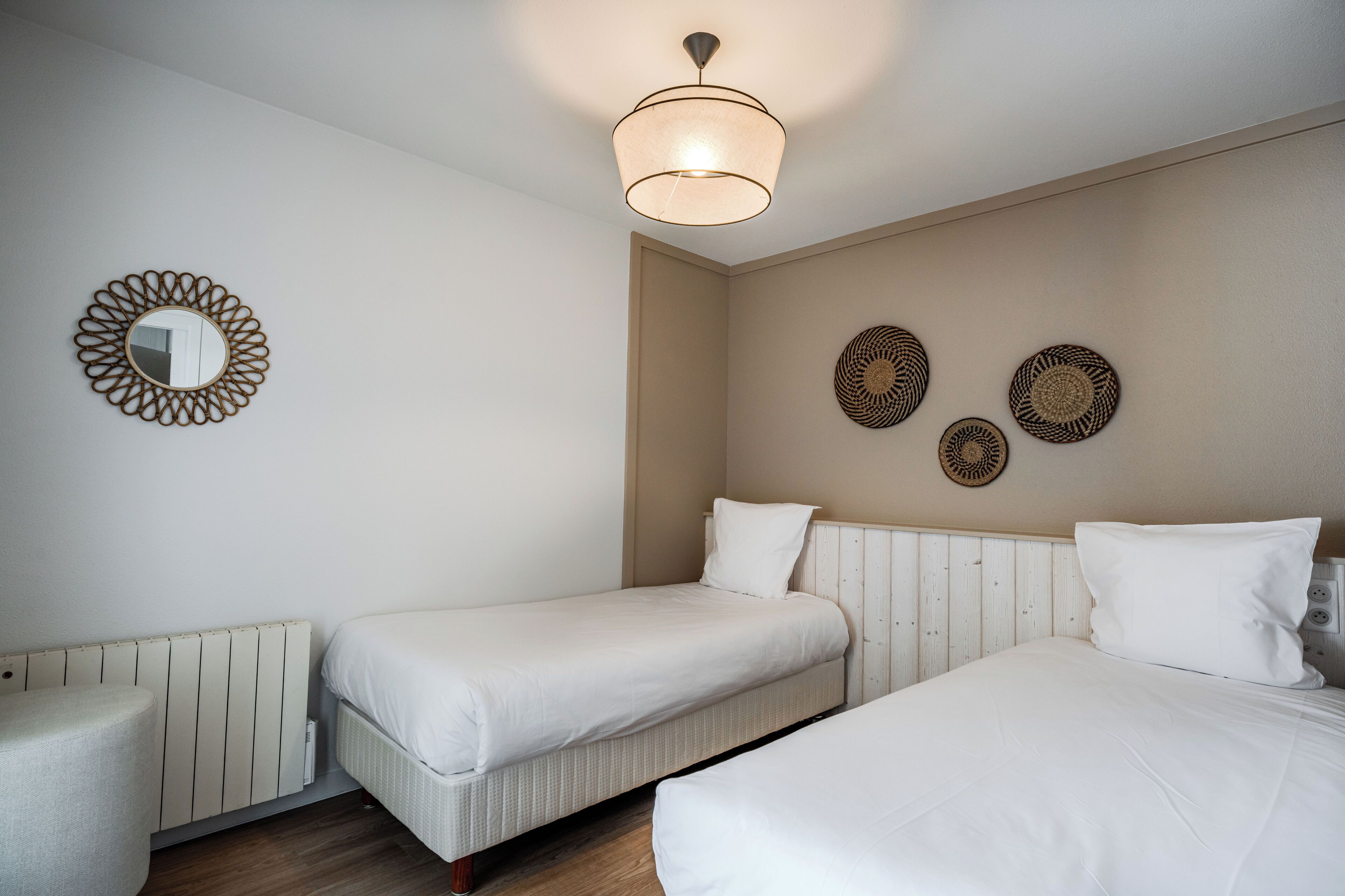 Et hotelværelse med to enkeltsenge, et rundt spejl og tre billeder på væggen.