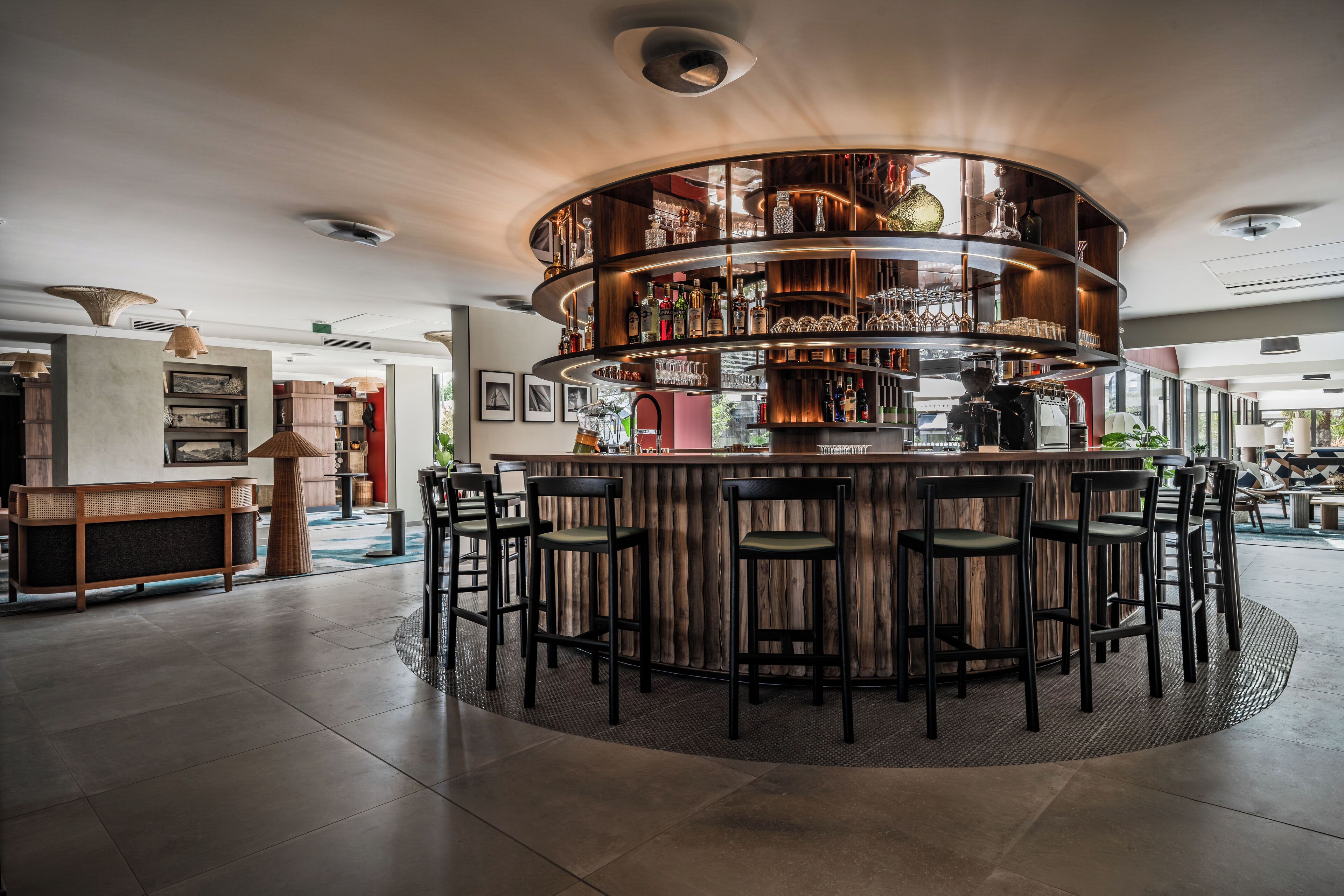 A bar area with a circular wooden bar, multiple seating options, and a variety of bottles and glasses on shelves.