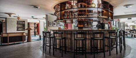 A bar area with a circular wooden bar, multiple seating options, and a variety of bottles and glasses on shelves.