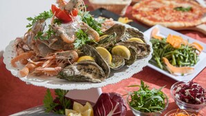 A seafood platter with shrimp, oysters, and lemon slices, accompanied by various salads and a pizza. - Hotel Bologna (Misano Adriatico)