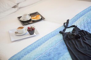 A neatly made bed with a blue quilt, a black garment, a tray with breakfast including toast, a cup of coffee, and a bowl of cherries. - Hotel Bologna (Misano Adriatico)