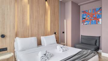 Ein modernes Hotelzimmer mit einem großen Bett, einem grauen Sessel, einem Gemälde an der Wand und einem Nachttisch mit einer Lampe.