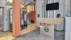 Zona de recepción de hotel con diseño moderno, que incluye un mostrador de recepción, un televisor montado y una máquina de café.