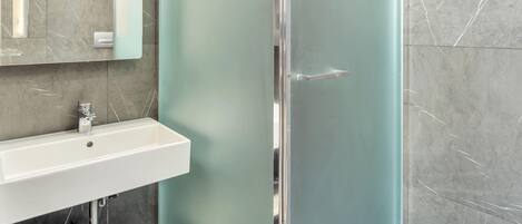A bathroom with a glass shower door, a white sink, and a mirror above it.