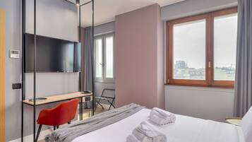 Una camera d'albergo moderna con un letto, una scrivania, una sedia e un'ampia finestra.