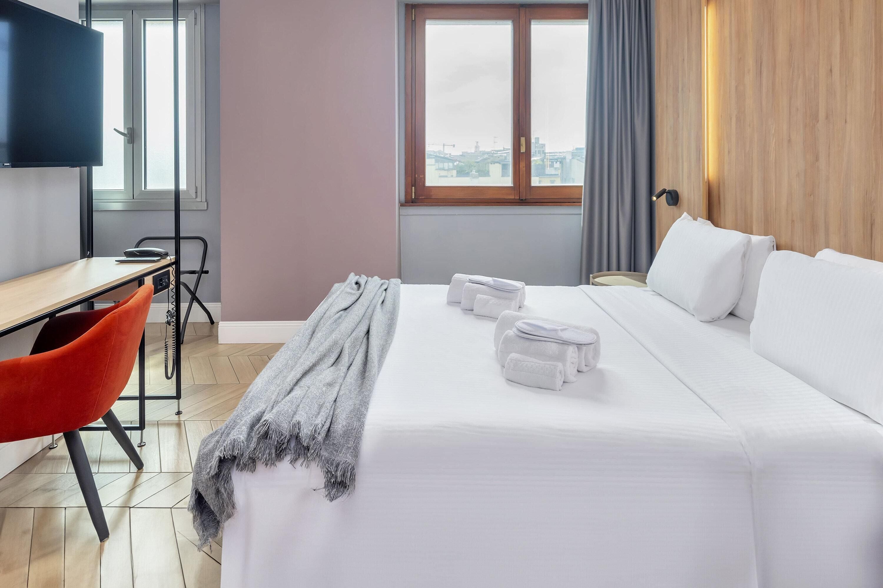 A hotel room with a bed, a desk, a chair, and a TV.