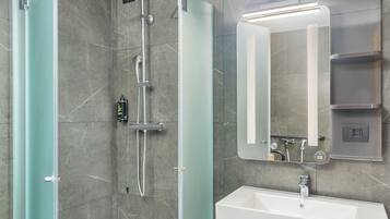 A modern bathroom with a glass-enclosed shower, a white sink, and a mirror with built-in lighting.