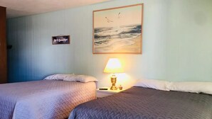 Habitación de hotel con dos camas, una mesita de noche con lámpara, un cuadro de pájaros y un cartel en la pared.