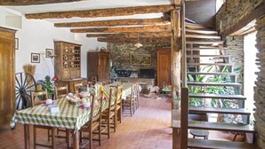 Un comedor rústico con mesas y sillas de madera, una pared de piedra y una escalera que lleva a un balcón con plantas.