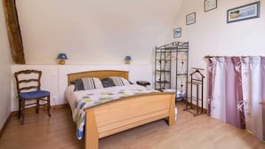 Un dormitorio con una cama de madera, una silla, una estantería metálica y una cortina estampada con motivos florales.