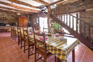 A rustic dining area with a checkered tablecloth, wooden chairs, and a stone wall backdrop. - Chambres d'Hotes La Ferme de Bizoin (Merleac)