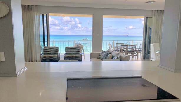 Une chambre d’hôtel moderne dotée d’une grande fenêtre donnant sur la mer et sur un bateau. On y trouve un coin salon avec deux fauteuils à motifs et un canapé.