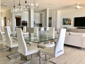 Une cuisine moderne avec des meubles blancs, des appareils en acier inoxydable et une table à manger en verre, assortie de chaises blanches.