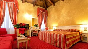 A hotel room with a red carpet, a bed with striped bedding, a desk with a chair, and a small table with a vase of flowers. - Ca' San Polo - Ferretti Hotels Collection (Venice)
