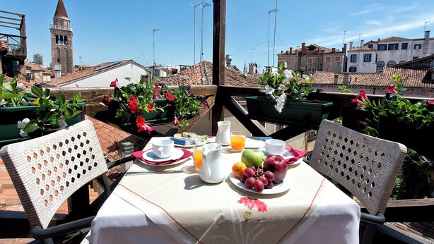 A rooftop terrace with a table set for breakfast, featuring a variety of fruits and a pitcher of orange juice. - Ca' San Polo - Ferretti Hotels Collection (Venice)