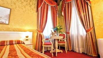 A hotel room with a bed, two chairs, a table with a vase, and curtains.