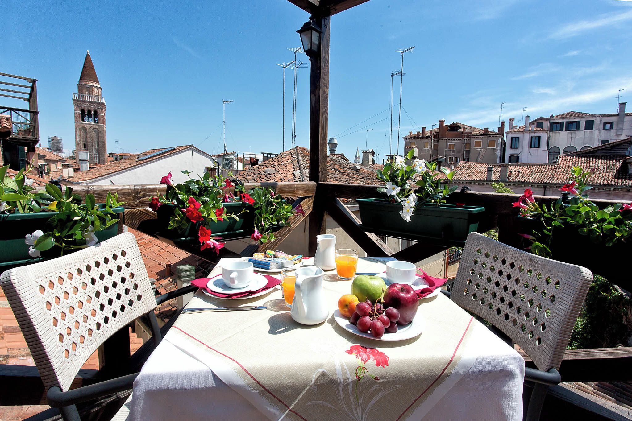 A rooftop terrace with a table set for breakfast, featuring a variety of fruits and a pitcher of orange juice.