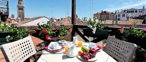 Terraza en la azotea con una mesa dispuesta para el desayuno, mostrando una variedad de frutas y una jarra de jugo de naranja.