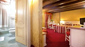A hotel room with a wooden ceiling, a red carpet, a bed with striped bedding, a desk with a chair, and a television. - Ca' San Polo - Ferretti Hotels Collection (Venice)