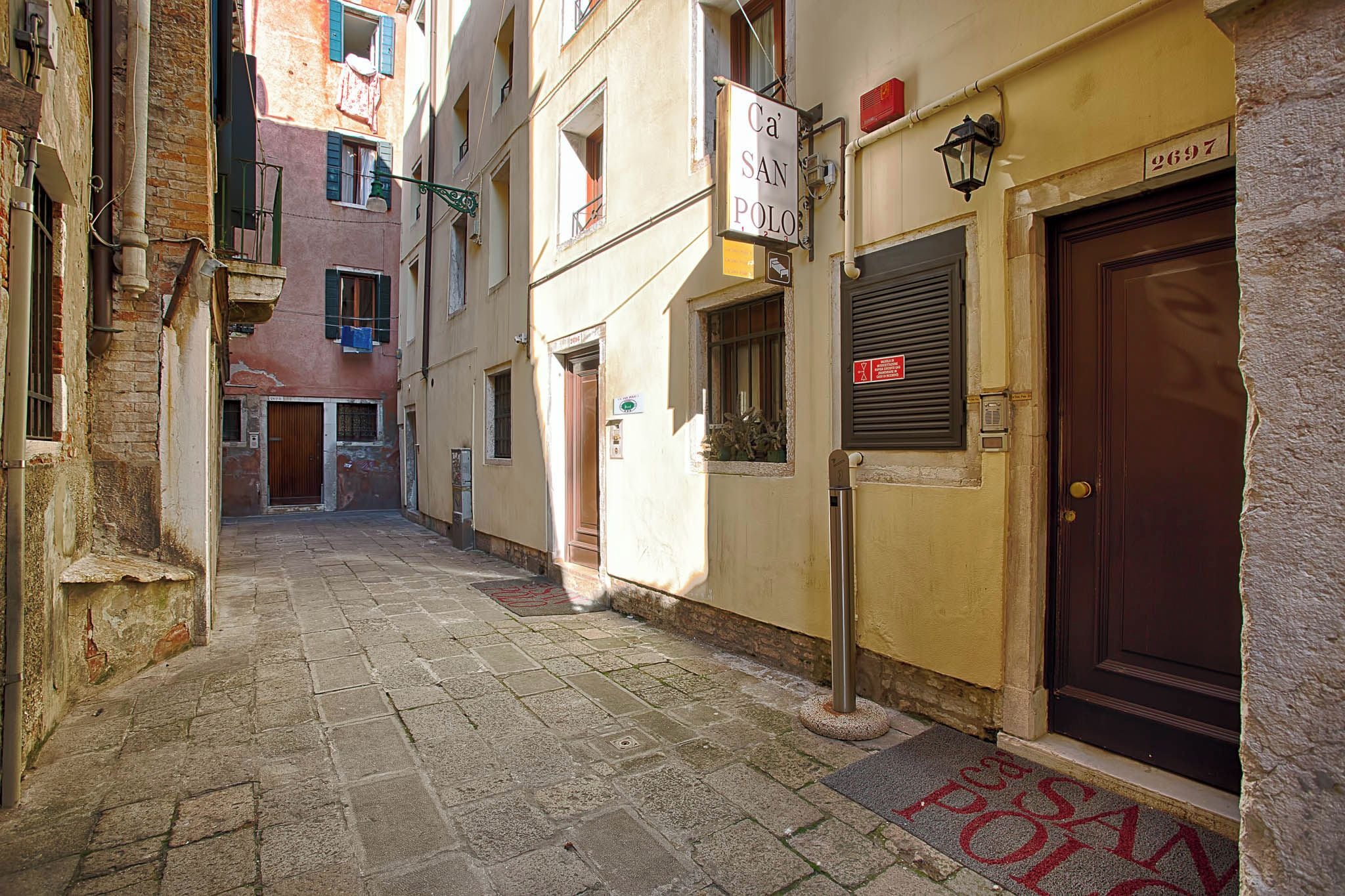 Uma rua estreita com um edifício identificado como 'Ca' San Polo' e uma porta com o número '2697'.