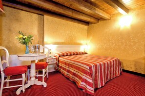A small room with a bed, a table with a vase of flowers, and a chair. - Ca' San Polo - Ferretti Hotels Collection (Venice)