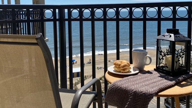 Ein Balkon mit Blick auf den Strand, ein Tisch mit einer Schüssel Essen, eine Tasse und eine Laterne.
