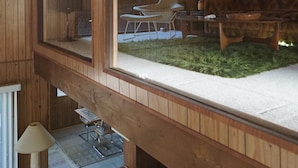 A wooden interior with a high ceiling, a dining area with a table and chairs, and a window overlooking a grassy area. - 1970s Architecture & Design Cabin - The Lone Pine (Frazier Park)